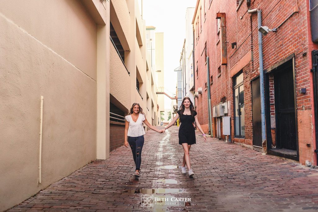 high school sisters holding hands in an alley